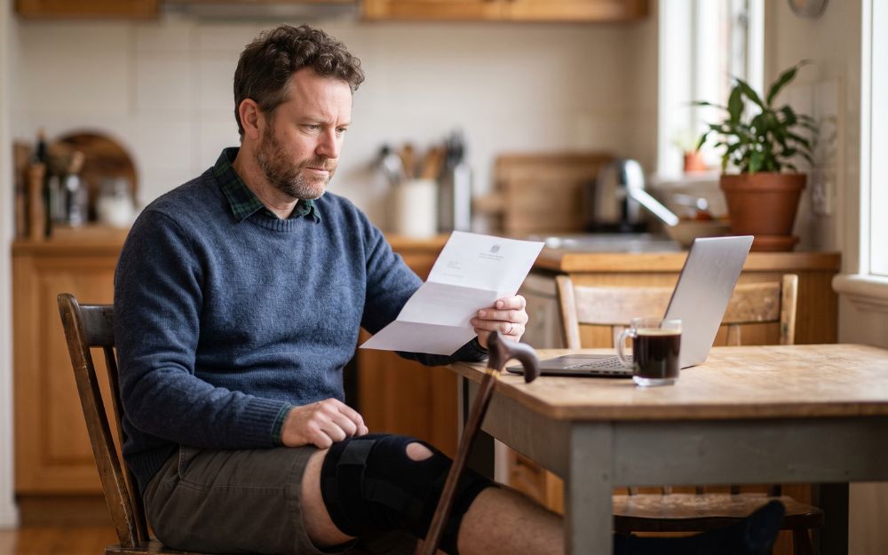 Man with a knee brace and cane reviewing a letter where his TPD claim rejected at home, considering his appeal options